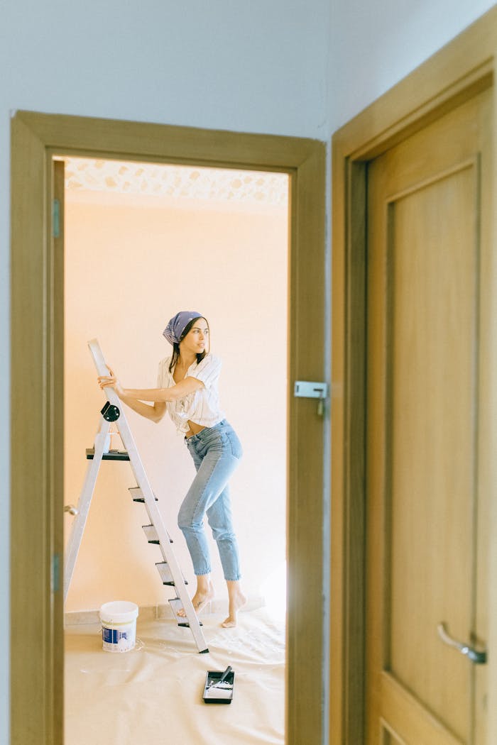 Young woman painting an indoor wall from a stepladder during home renovation.